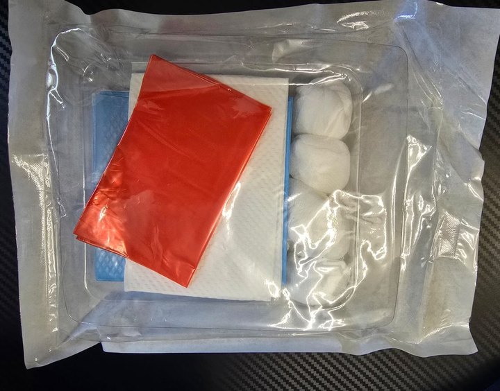 The tray inside the dressing kit: drape, towels, gauze balls and swabs under the film